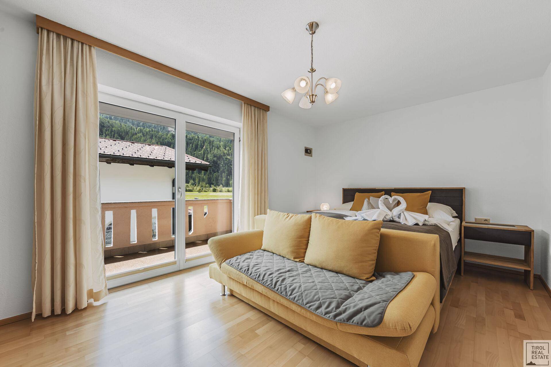 Helles Schlafzimmer mit Holzboden, Schlafsofa und Zugang zum Balkon.
