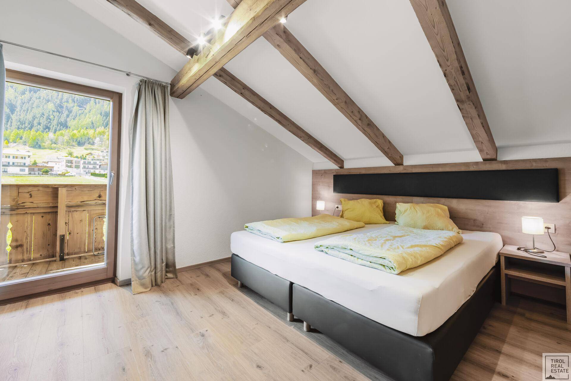 Helles Schlafzimmer im Dachgeschoss mit Holzbalken, Doppelbett und Balkonzugang.