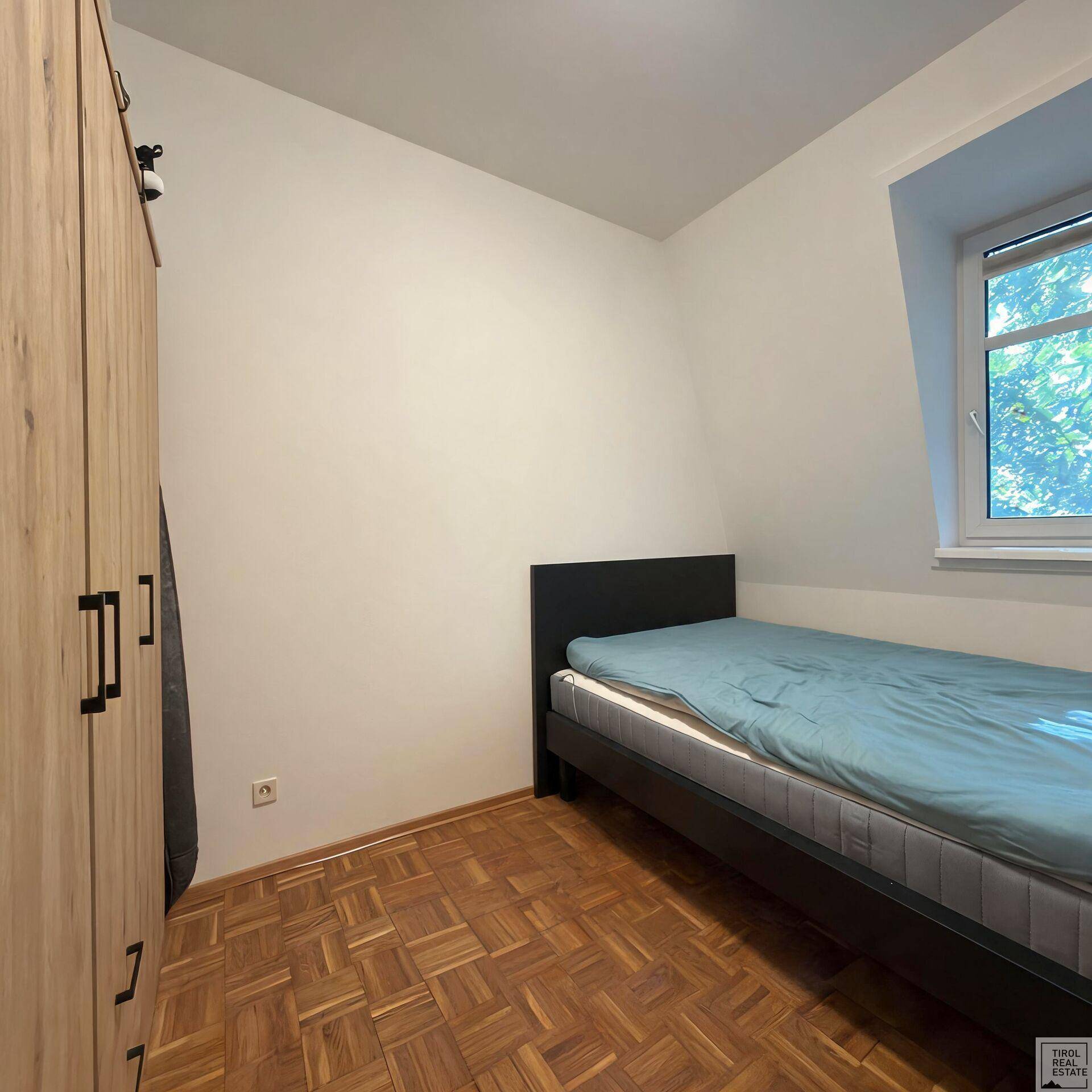 Gemütliches Schlafzimmer mit Einzelbett, Kleiderschrank und Parkettboden unter einer Dachschräge.