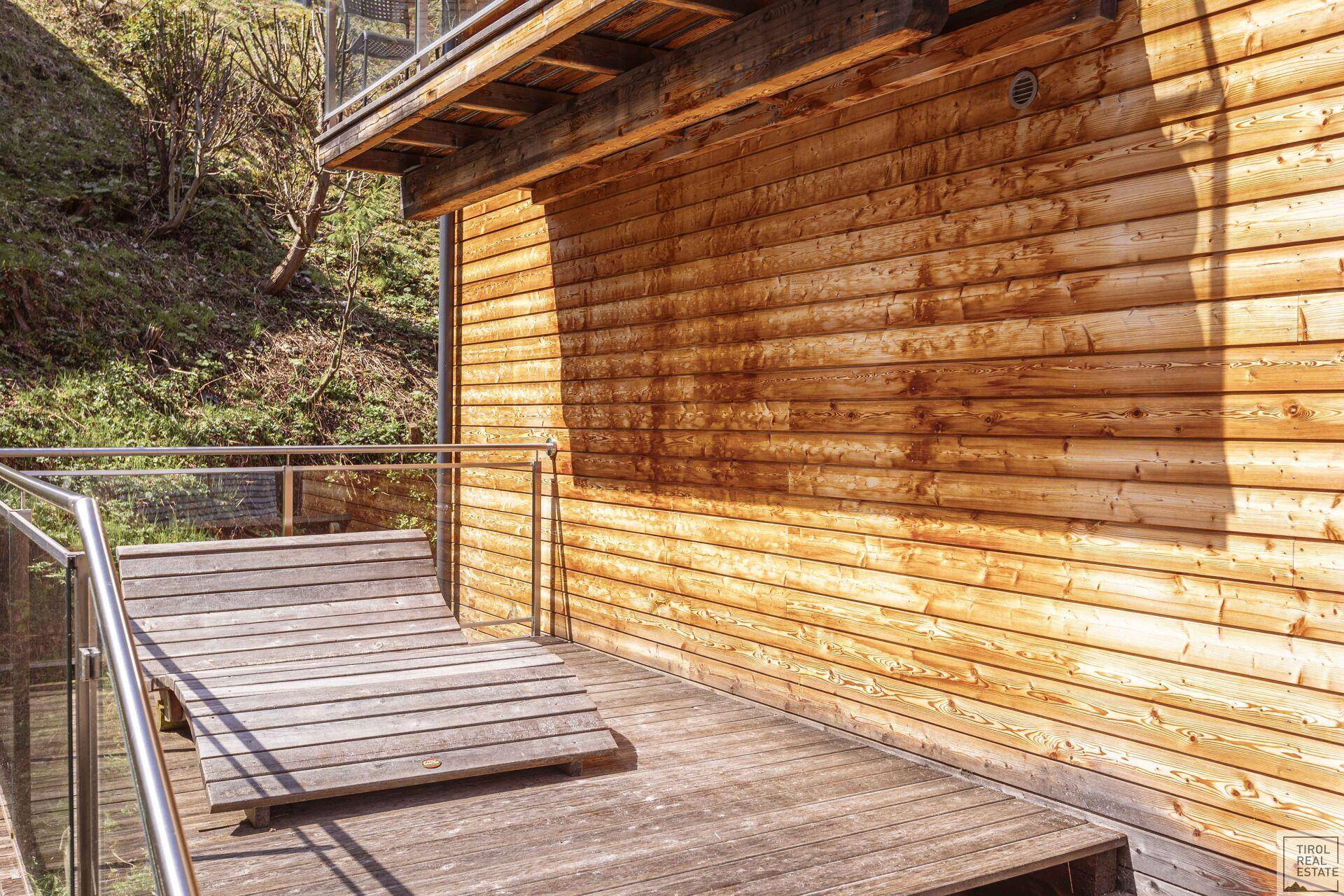 Holzterrasse neben der Fassade eines Holzchalets in sonniger Lage.