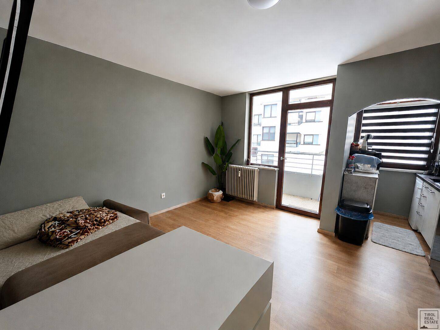 Helles Wohnzimmer mit Holzboden, Sofa und Zugang zu einem Balkon.