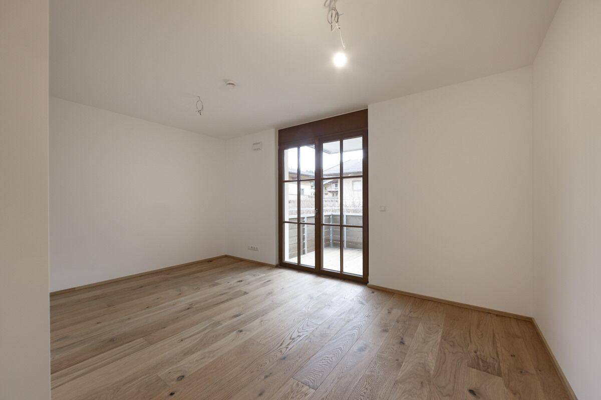 Geräumiger Raum mit Eichenparkett und Balkonzugang, ideal für ein Schlafzimmer.