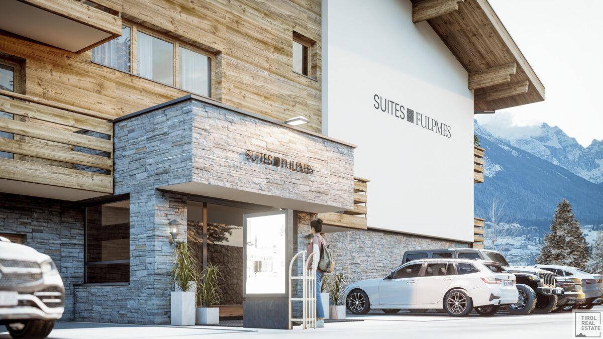 Eingangsbereich eines modernen Gebäudes im alpinen Stil mit Steinverkleidung und verschneiter Bergkulisse.