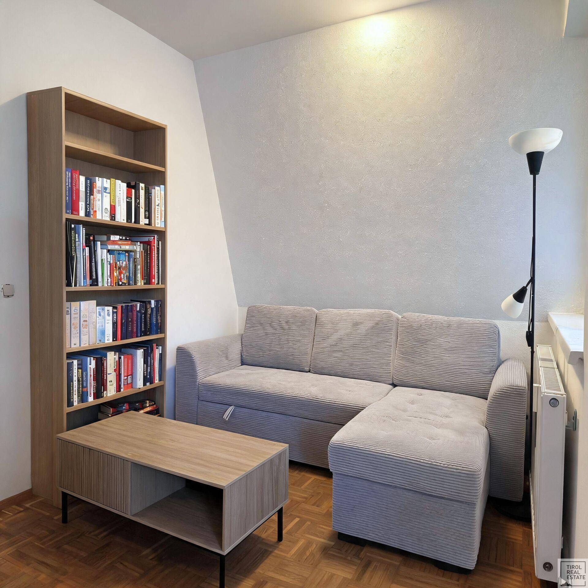Gemütliches Wohnzimmer mit Sofa, Couchtisch, Bücherregal und Parkettboden unter einer Dachschräge.