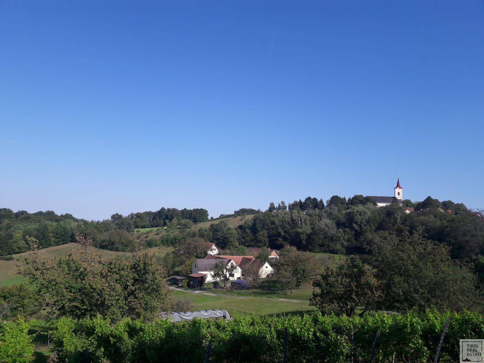 Weitläufige grüne Landschaft mit einem Dorf und einer Kirche in der Ferne unter klarem Himmel.