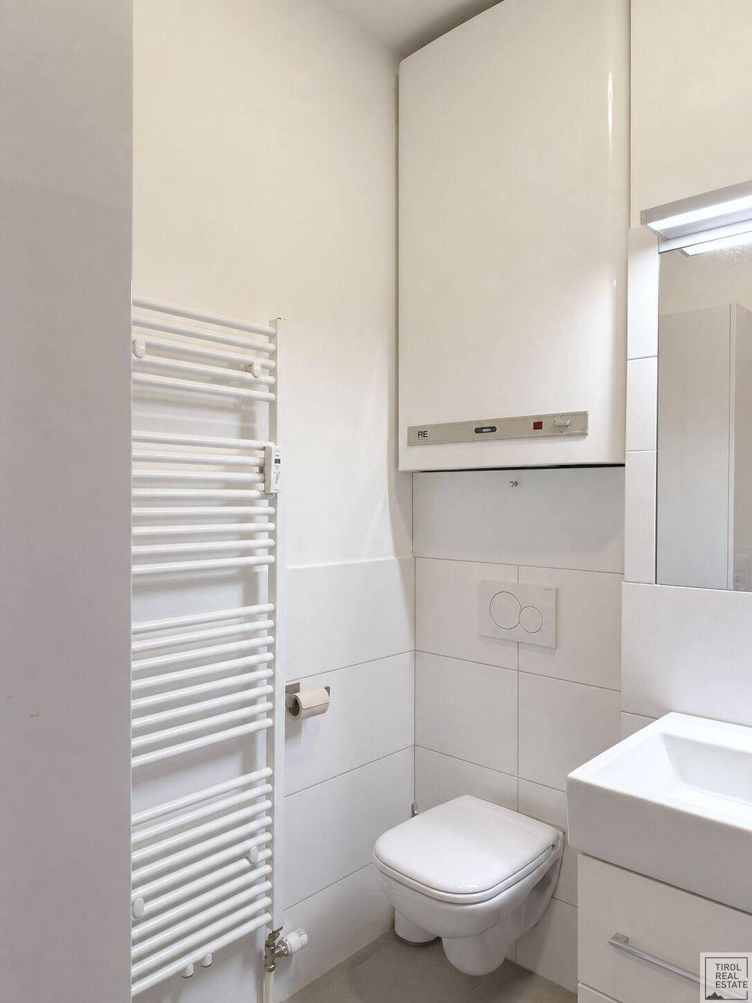 Helles Badezimmer mit WC, Waschbecken, Spiegelschrank und einem praktischen Handtuchheizkörper.