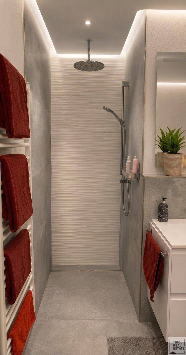 Elegante Duschkabine mit Regendusche, modernen grauen Fliesen und indirekter Beleuchtung für Wellness-Gefühl.