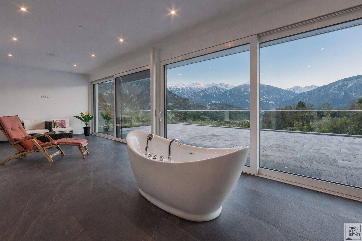 Luxuriöses Badezimmer mit freistehender Badewanne und Zugang zu einer großen Terrasse mit Bergblick.