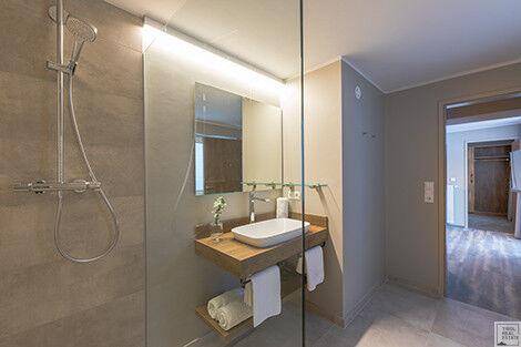 Modernes Badezimmer mit ebenerdiger Dusche, stilvollem Waschbecken und Holzablage.