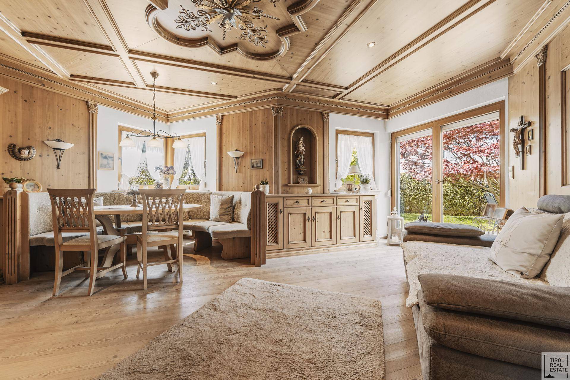 Traditionelles Wohnzimmer mit Holztäfelung, geschnitzter Decke und gemütlicher Sitzecke mit Gartenblick.