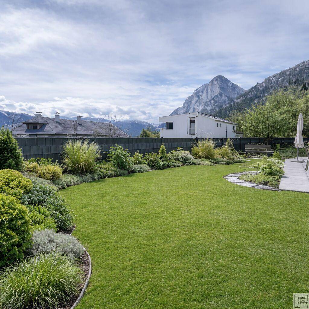 Gepflegter Garten mit Rasenfläche, Sträuchern und Bergblick im Hintergrund.