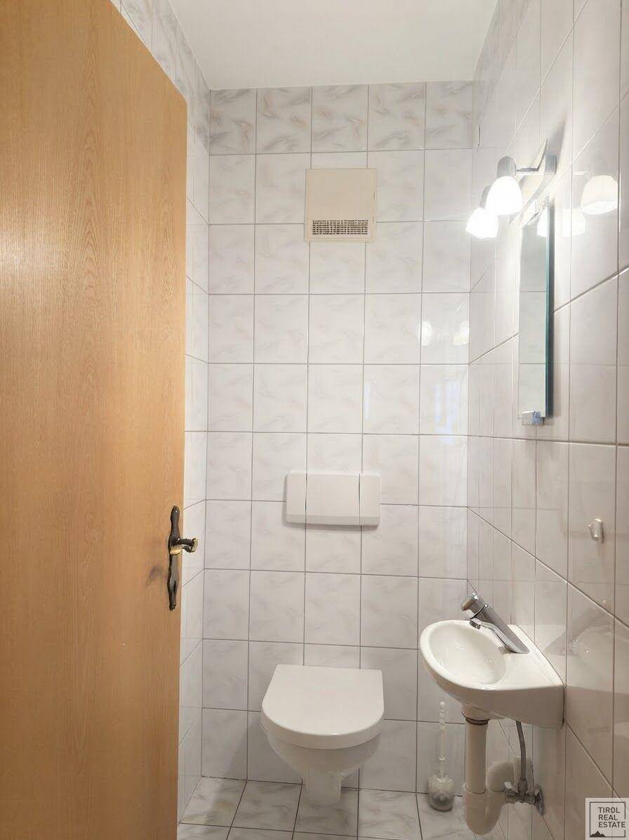 Kleines WC mit weißen Fliesen, Toilette und Handwaschbecken.