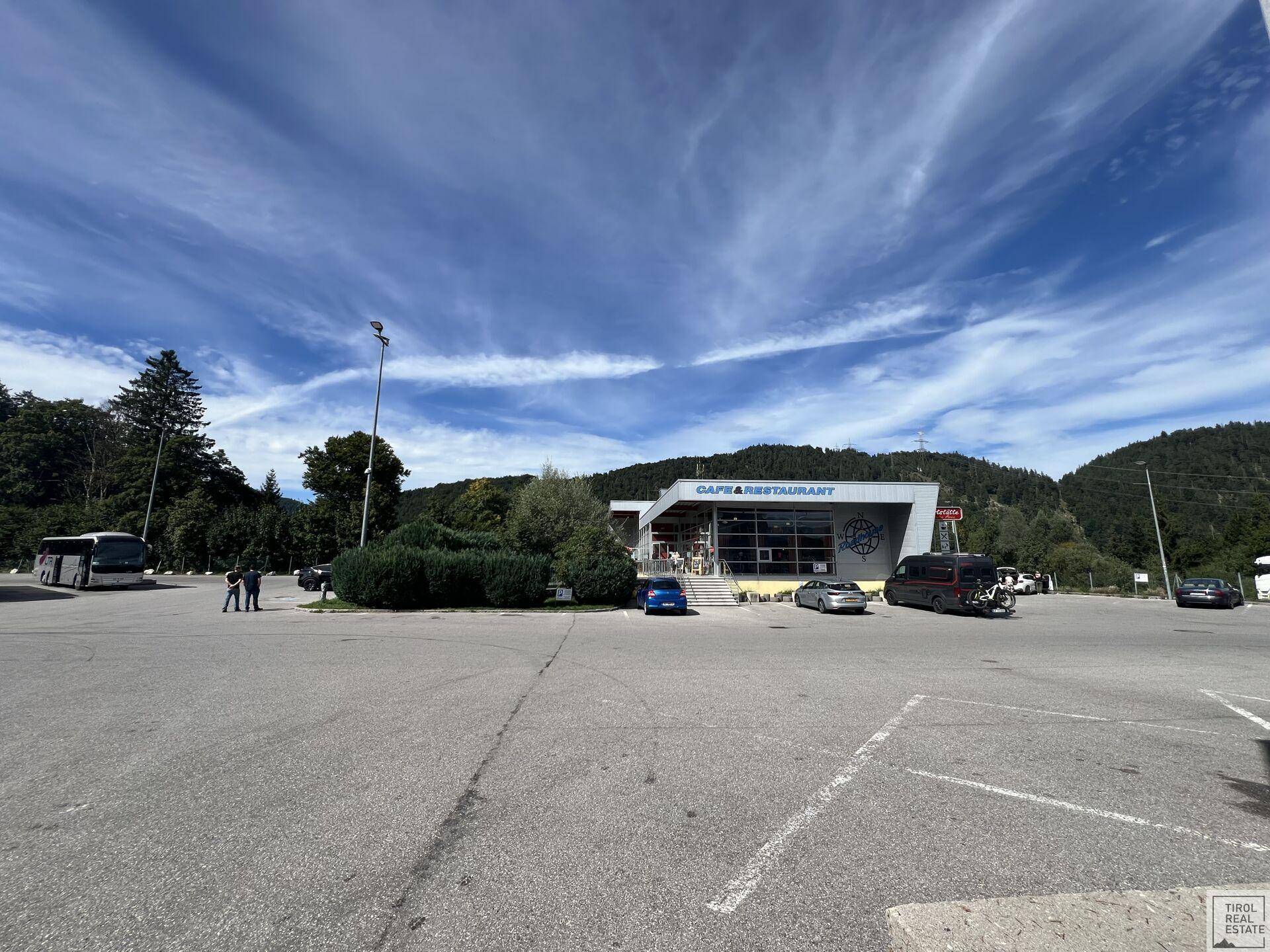 Weitläufige Außenansicht des Gebäudes mit großem Parkplatz und der beeindruckenden Bergkulisse.