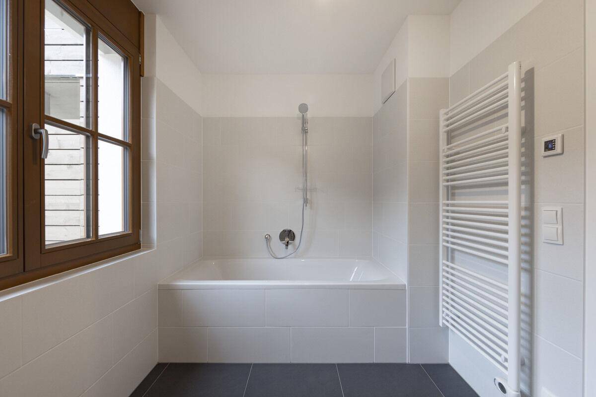 Modernes Badezimmer mit Badewanne, Duschfunktion, Fenster und beheiztem Handtuchhalter.