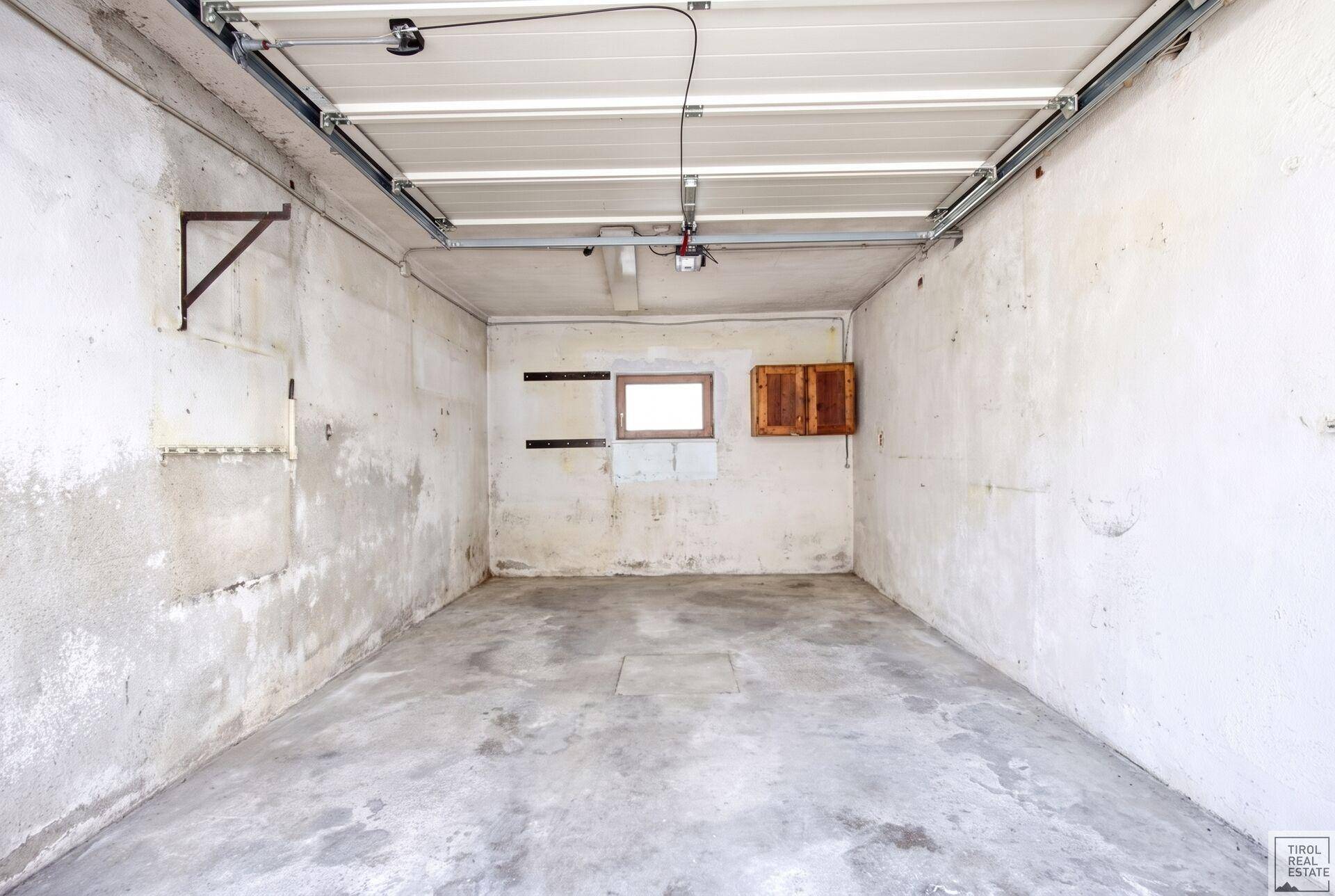 Leere Garage mit Betonboden und Rolltor, bereit zur Nutzung.