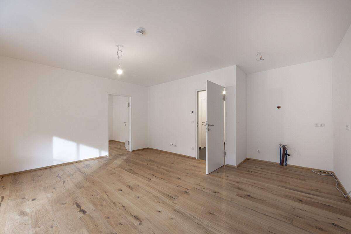 Geräumiger, unmöblierter Raum mit hellem Holzboden und weißen Wänden, ideal für ein Wohnzimmer.