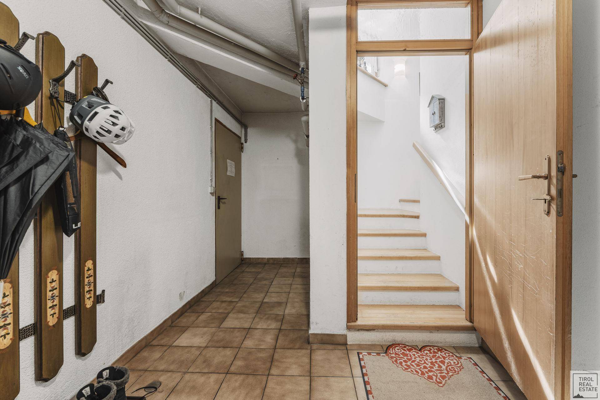 Kellerflur mit Fliesenboden, Holztreppe und Stauraum für Sportausrüstung.