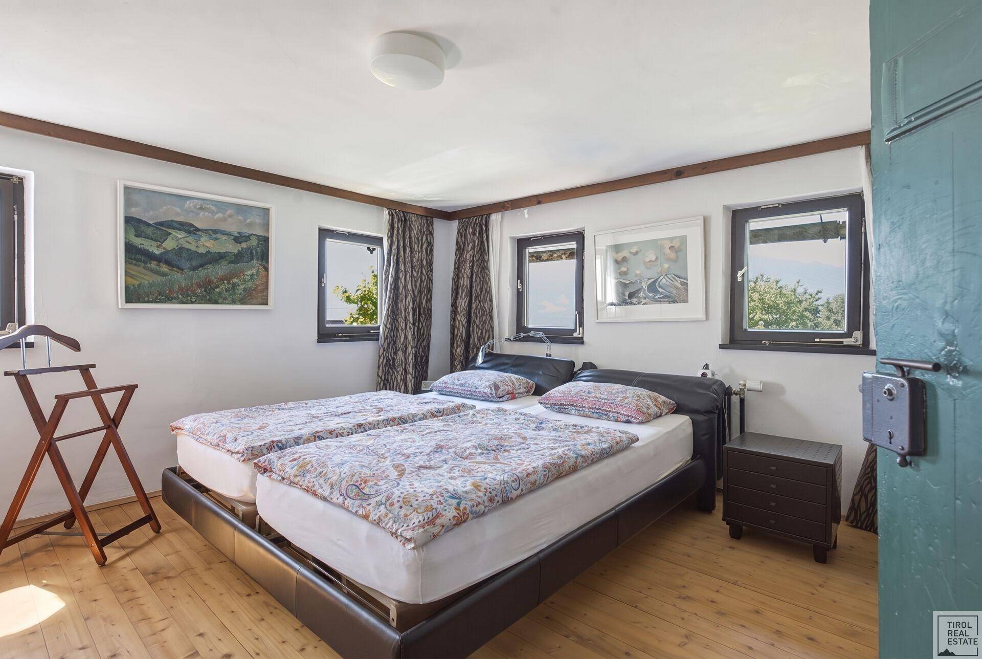 Helles Schlafzimmer mit Holzdielenboden, mehreren Fenstern und Bergblick.
