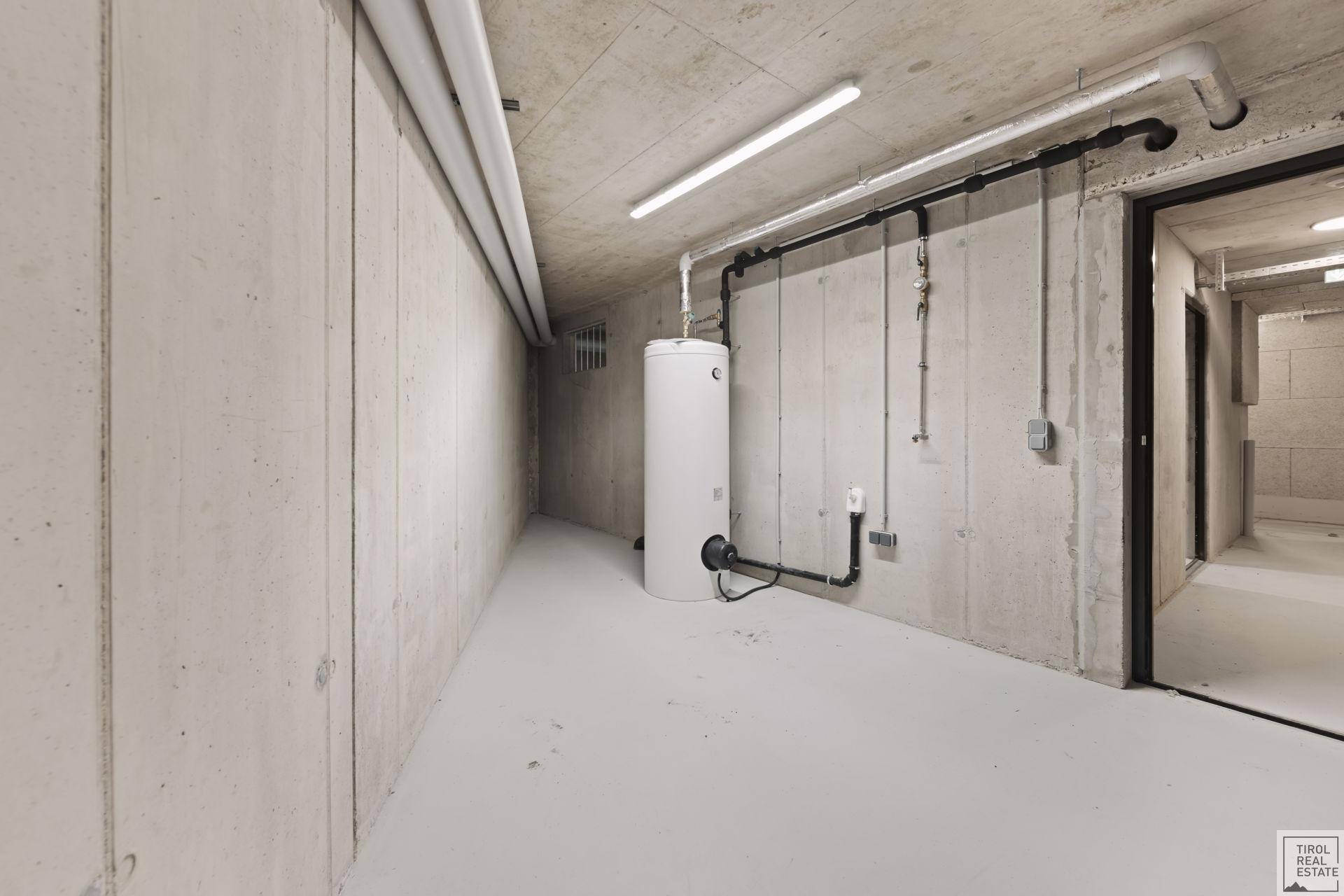 Kellerraum mit Betonwänden, Warmwasserspeicher und sichtbaren Leitungen.