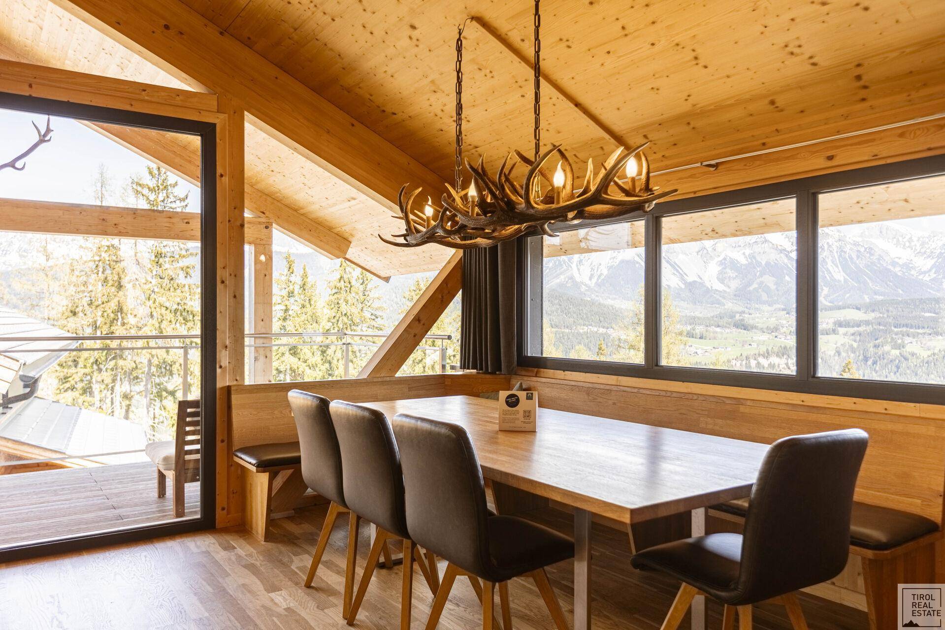 Essbereich mit Holztisch, Sitzbank und Bergblick durch große Fenster.