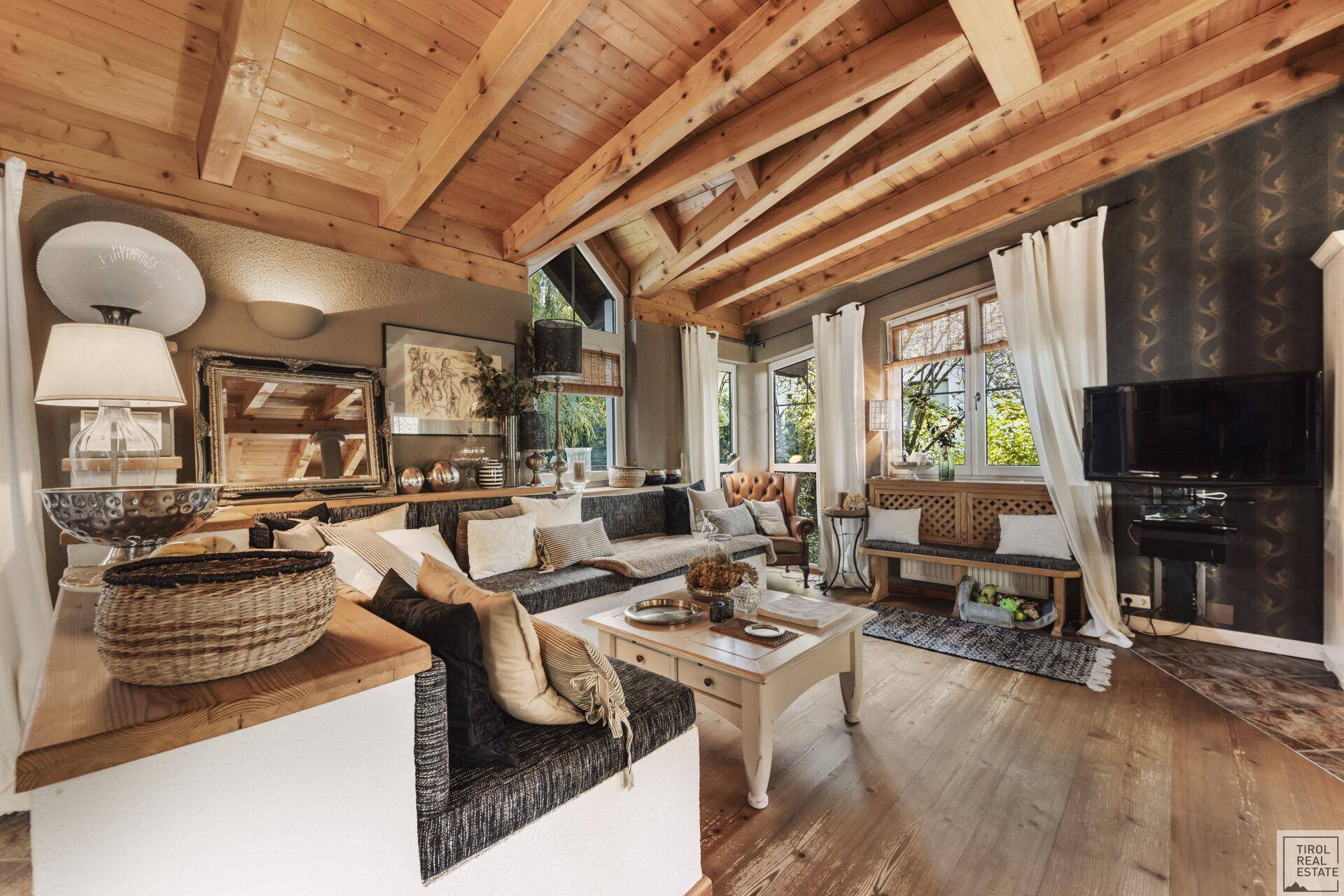 Stilvolles Wohnzimmer mit Holzbalkendecke, bequemer Sitzecke und vielen Fenstern für natürliches Licht.