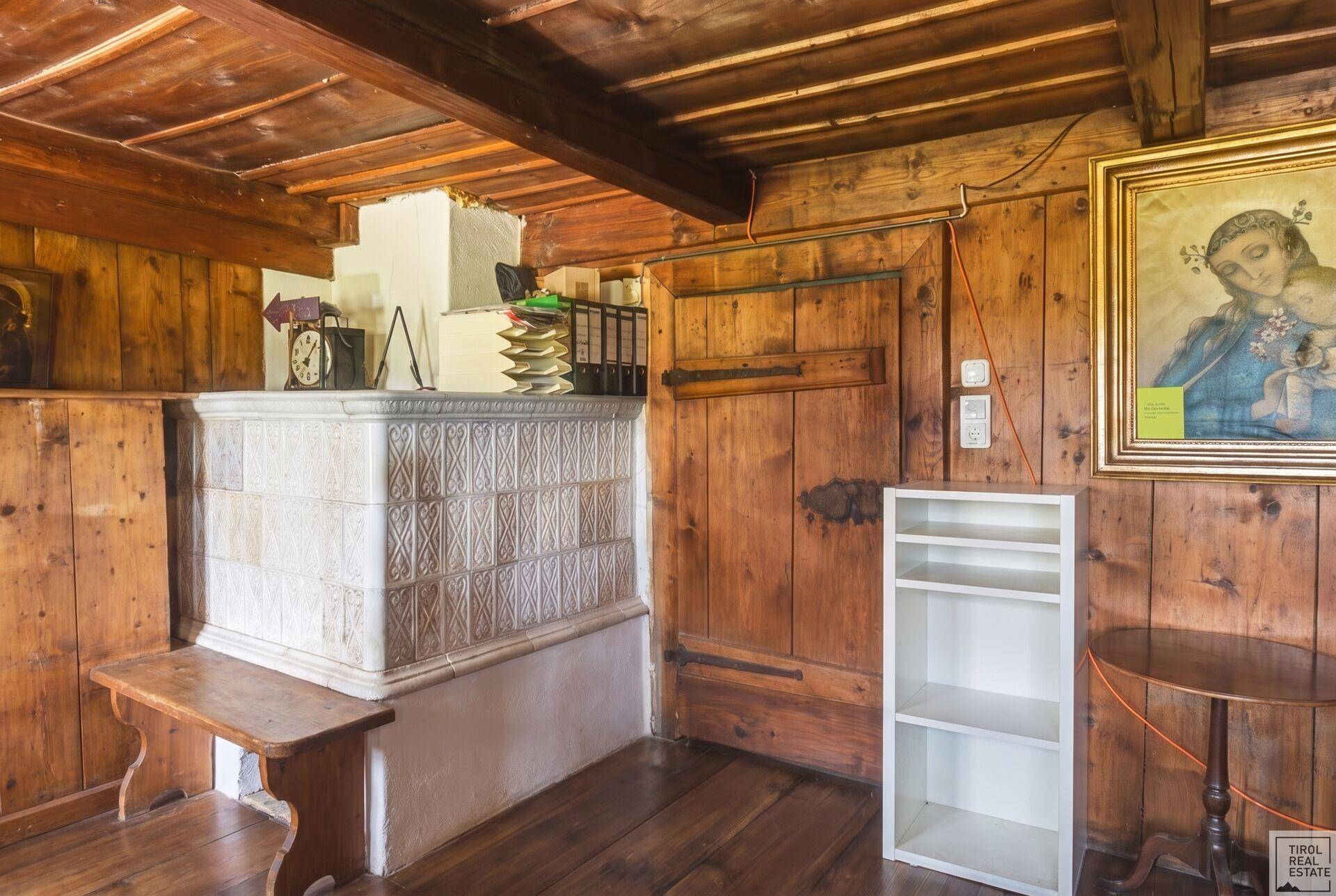 Rustikaler Wohnraum mit Kachelofen, Holzvertäfelung und Holzbalkendecke.