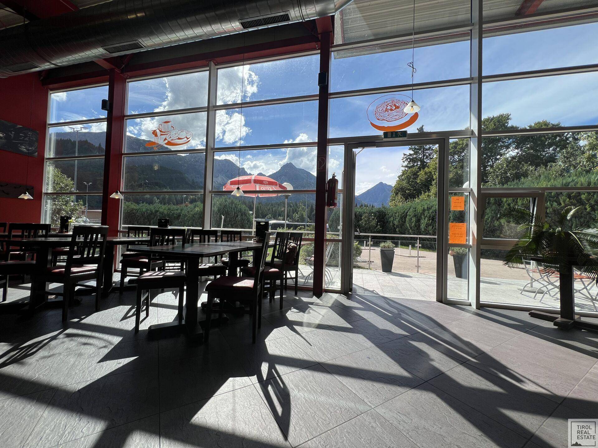Sonniger Restaurantbereich mit raumhohen Fenstern, die einen weiten Blick auf die Berglandschaft bieten.