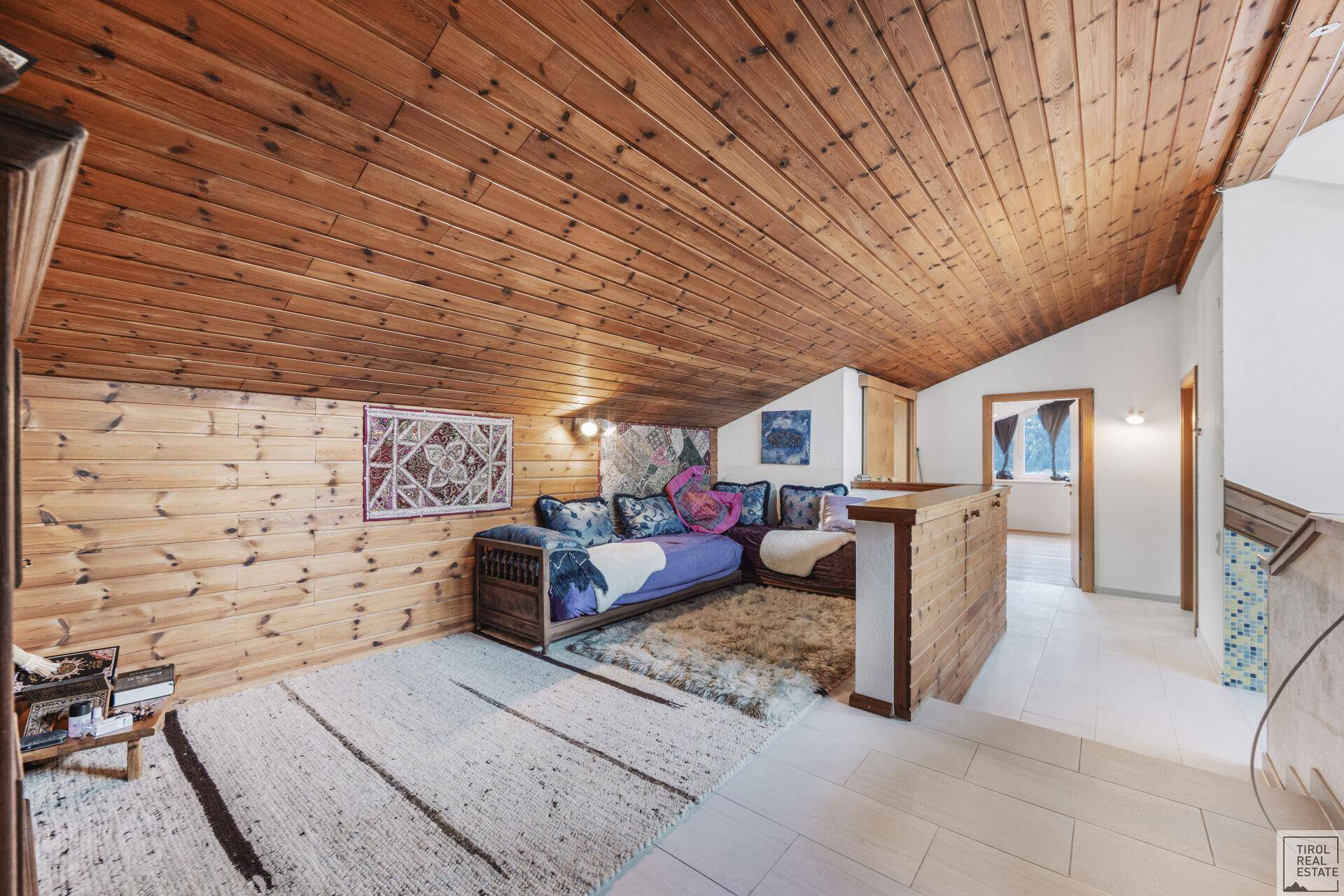 Gemütlicher Dachbodenbereich mit Holztäfelung, Teppichboden und Sitzgelegenheiten.