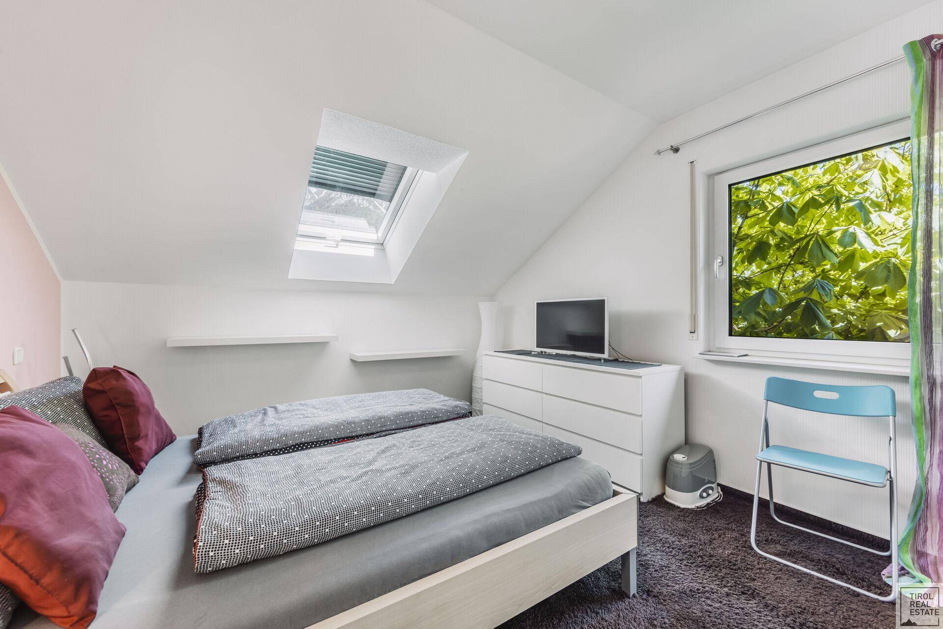Gemütliches Schlafzimmer im Dachgeschoss mit Dachfenster, Teppichboden und Blick ins Grüne.
