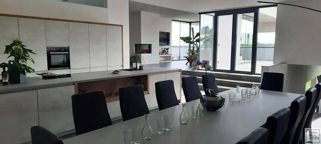 Moderner Essbereich mit langem Tisch und Stühlen, angrenzend an eine helle Einbauküche mit integrierten Geräten.