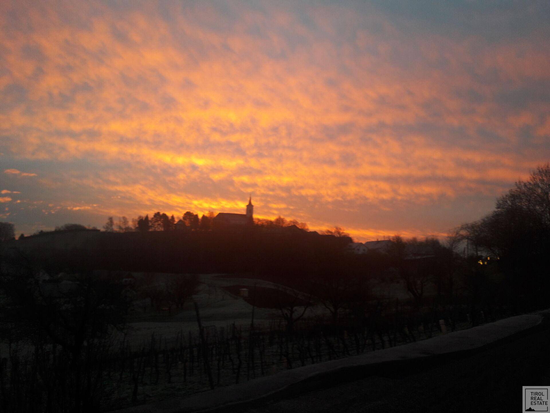Dramatischer Sonnenuntergang über einer hügeligen Landschaft mit einem Dorf und einer Kirche.