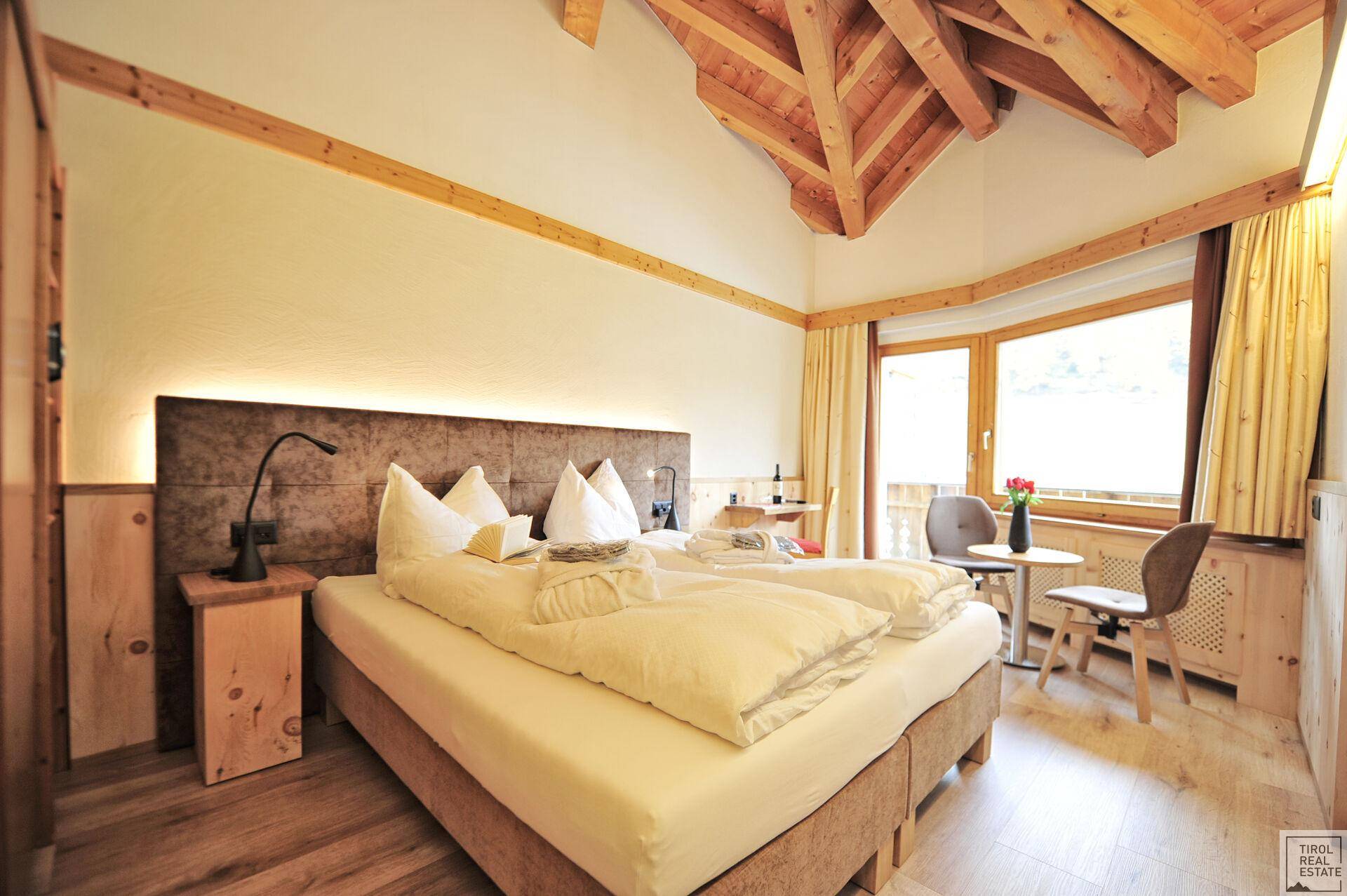 Gemütliches Schlafzimmer mit Holzbalkendecke, großem Bett und Blick auf die umliegende Natur.