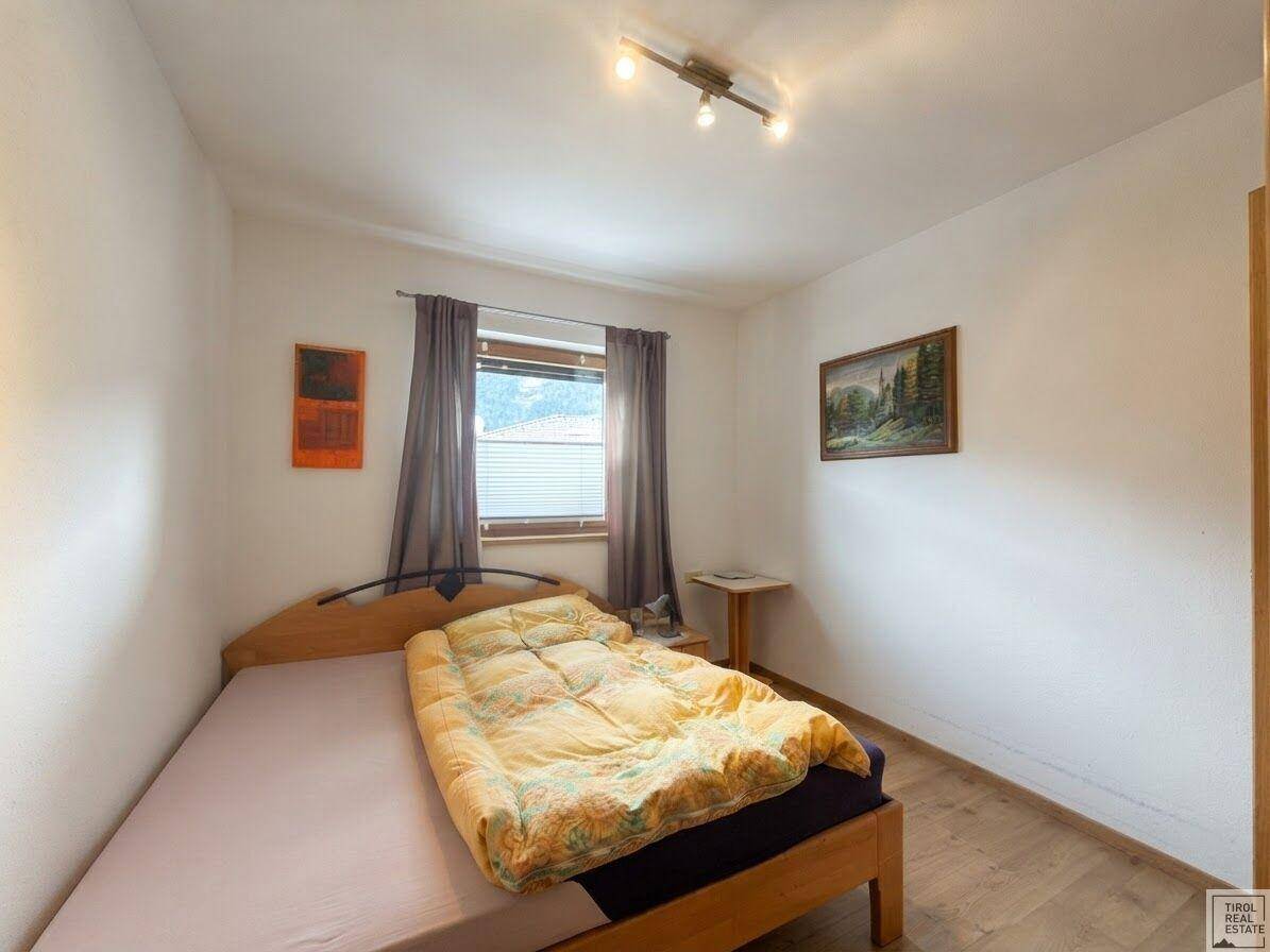 Gemütliches Schlafzimmer mit Holzbett, Parkettboden und Fenster mit Jalousien.
