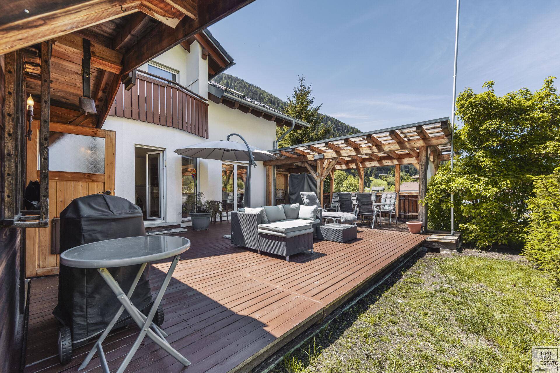 Weitläufige Holzterrasse mit überdachtem Essbereich und Blick auf die umliegende Landschaft.