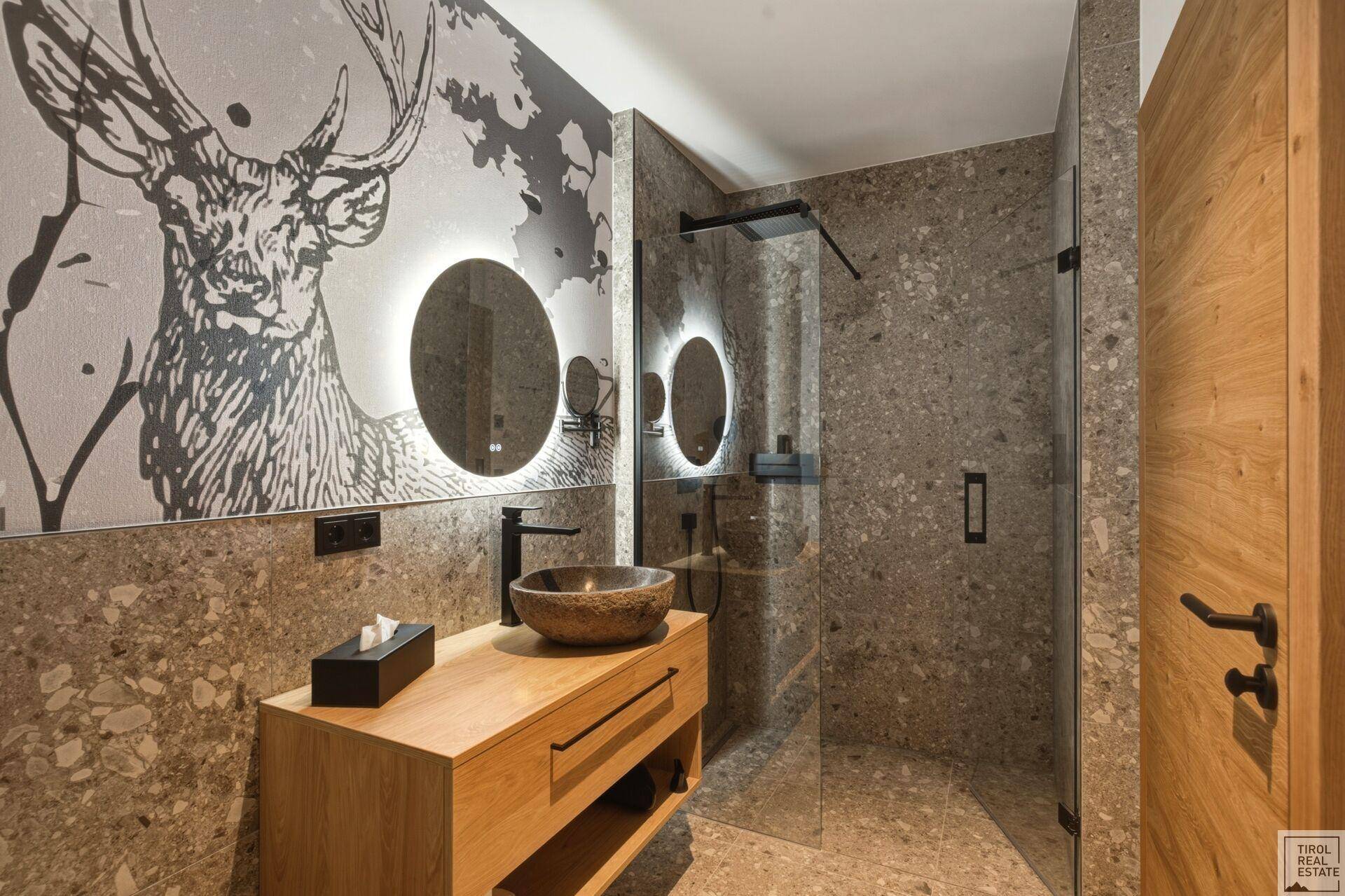 Elegantes Badezimmer mit begehbarer Dusche, Steinwaschbecken und beleuchteten Spiegeln.