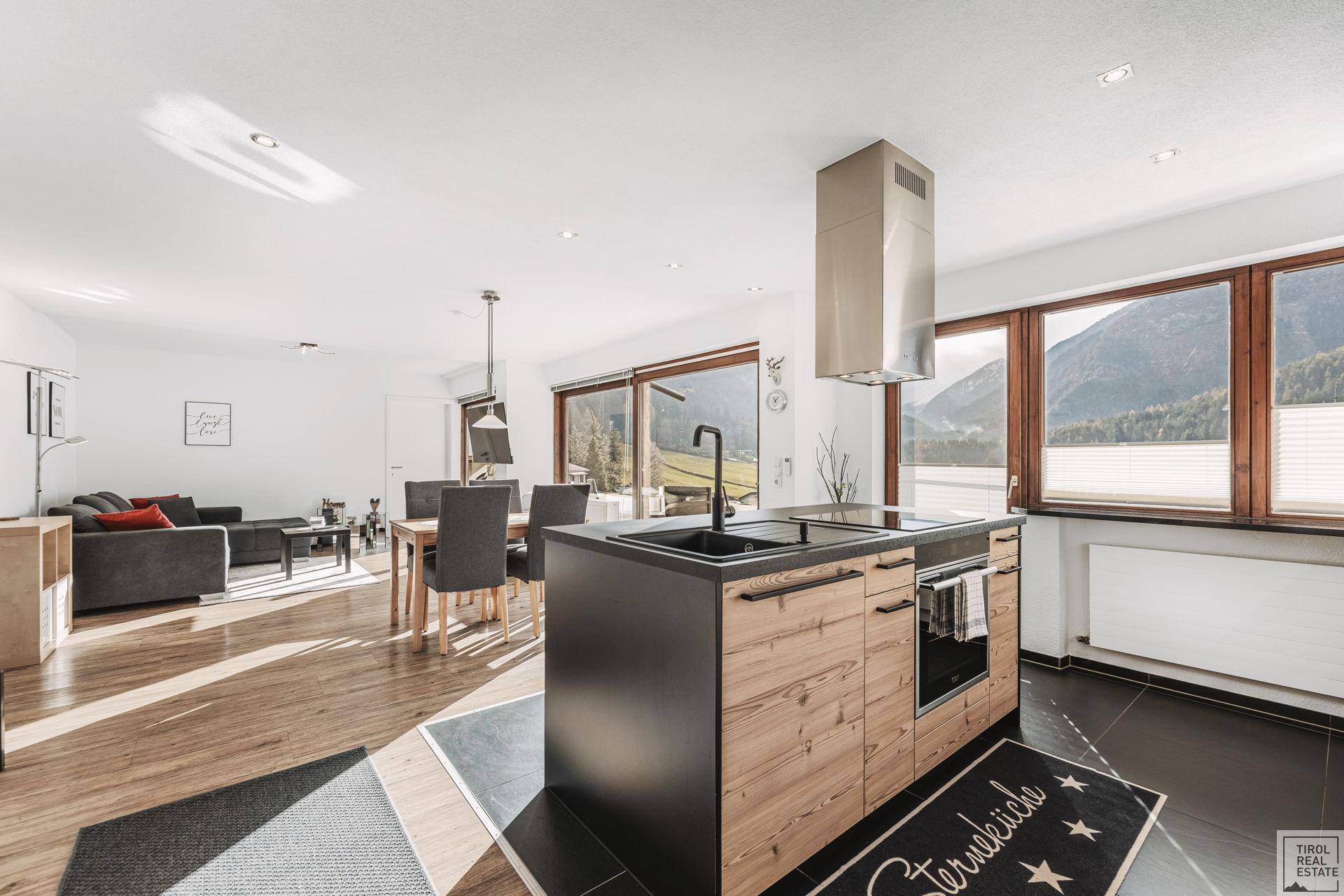 Moderne Küche mit Kochinsel und Essbereich, offen zum Wohnzimmer mit Bergblick.