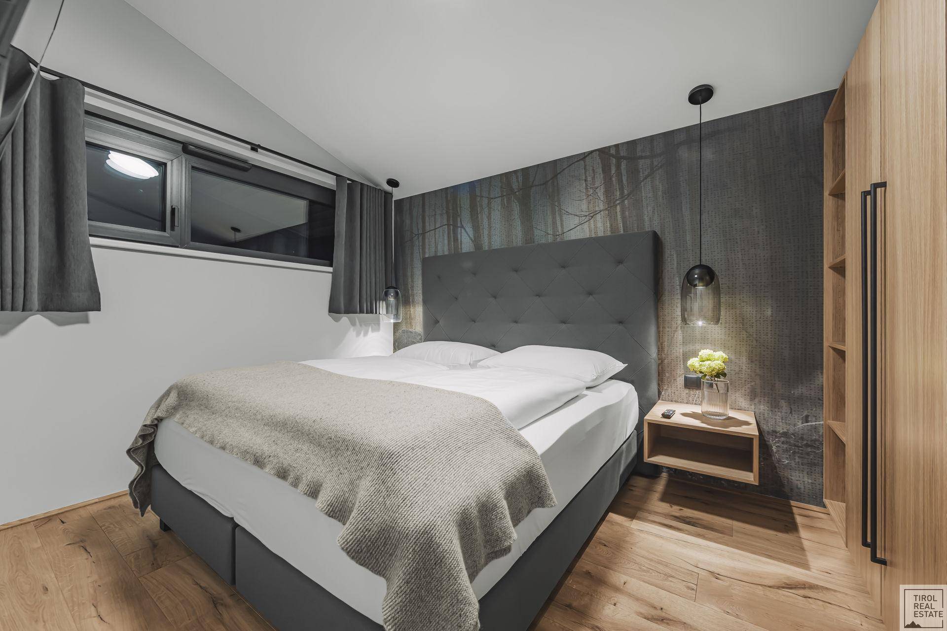 Modernes Schlafzimmer mit Doppelbett, Holzboden und stilvoller Wandtapete mit Waldmotiv.