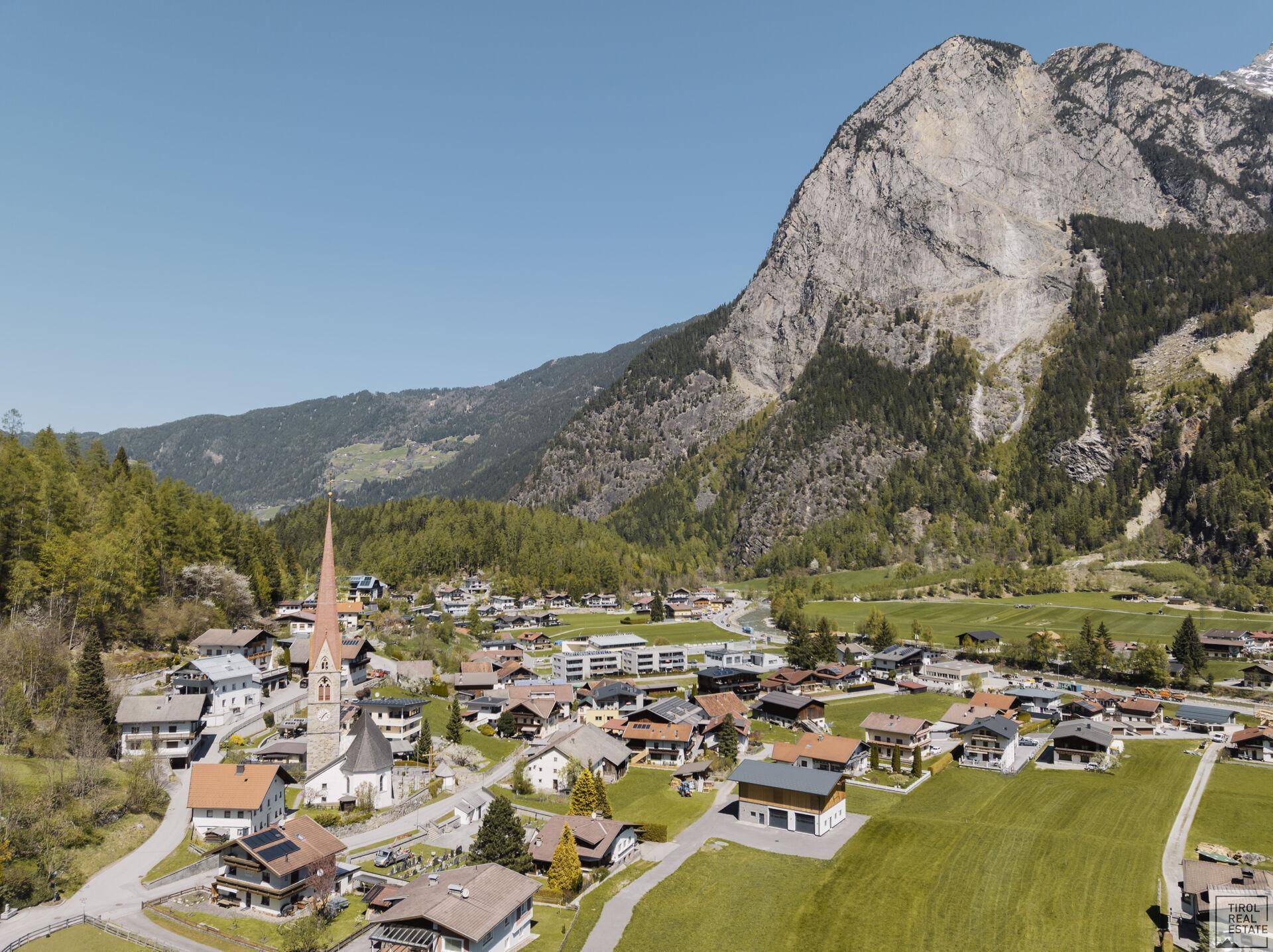 Weitläufige Luftaufnahme eines idyllischen Bergdorfes mit Kirche und umliegender Natur.