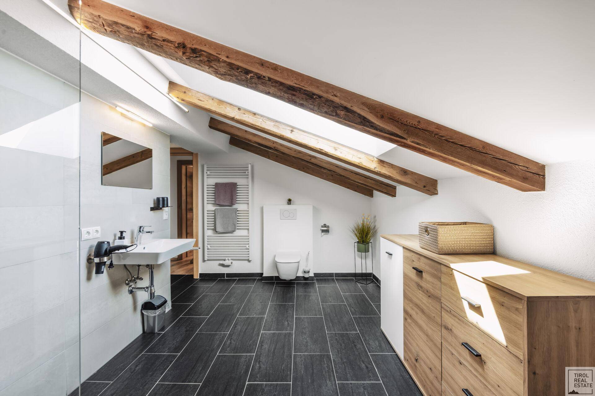 Geräumiges Dachgeschoss-Badezimmer mit ebenerdiger Dusche, Holzbalken und Dachfenster.