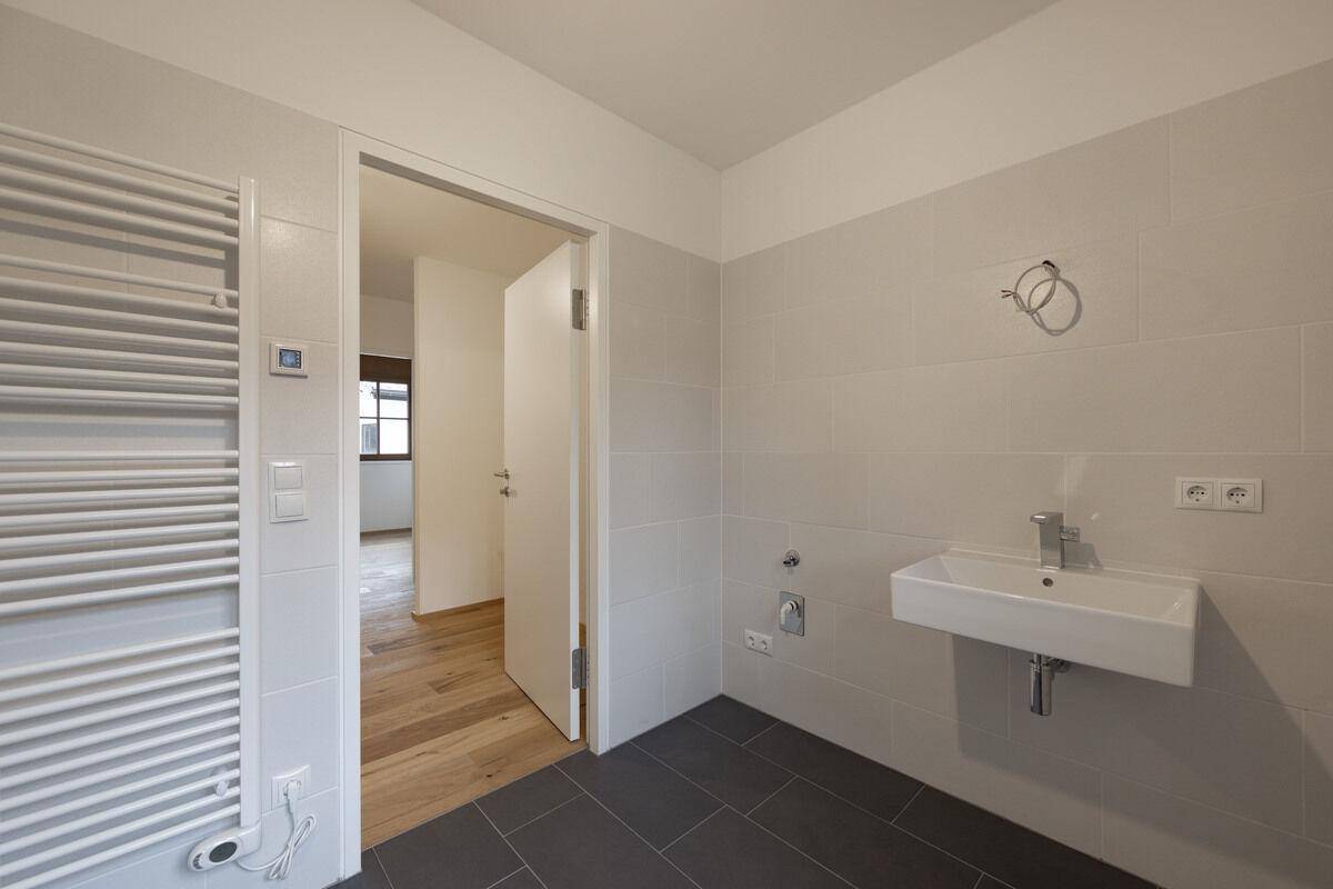 Funktionales Badezimmer mit Waschtisch, beheiztem Handtuchhalter und Zugang zu einem weiteren Raum.