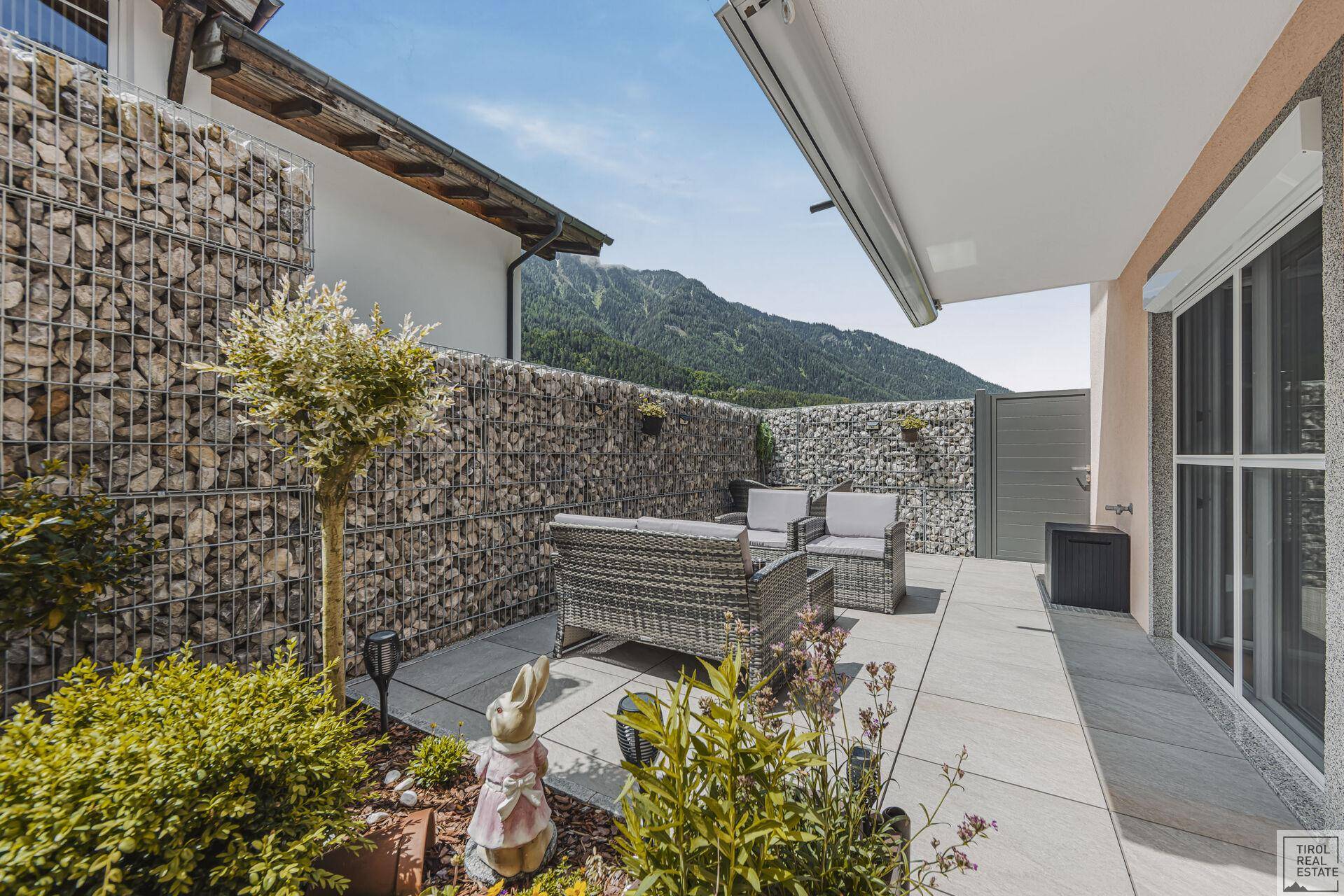 Sonnige Terrasse mit Gartenmöbeln, Pflanzen und Blick auf die Berge.