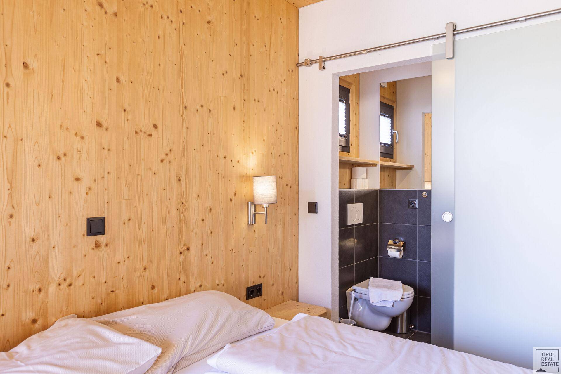 Schlafzimmer mit Holzwänden und Schiebetür zu einem separaten WC.