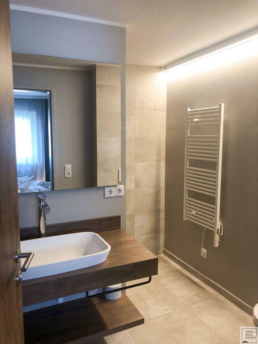 Funktionales Badezimmer mit modernem Waschbecken, großem Spiegel und beheiztem Handtuchhalter.