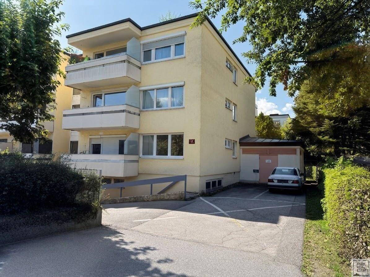 Mehrfamilienhaus mit Balkonen und Außenparkplätzen, umgeben von viel Grün.