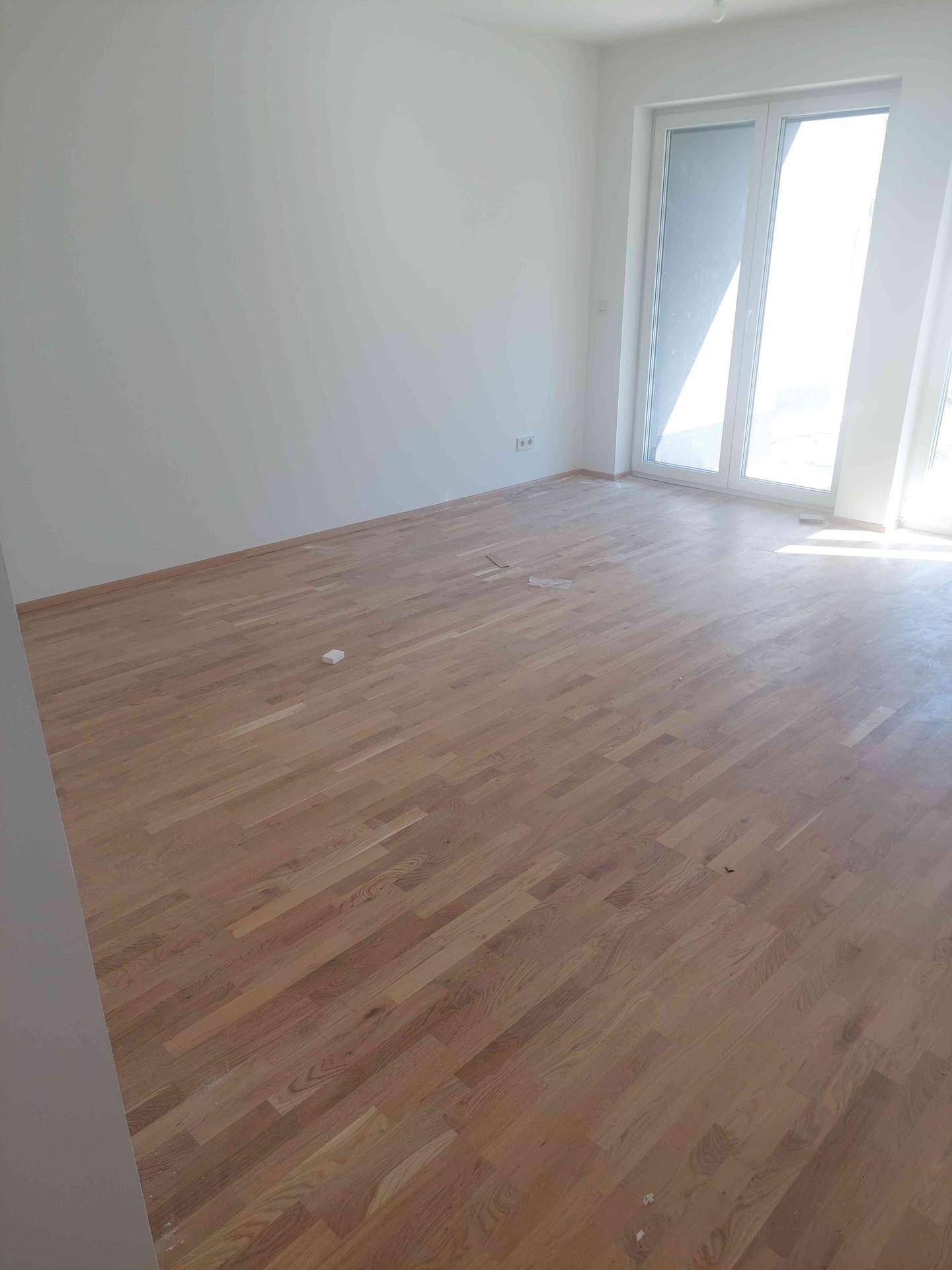 Heller, leerer Raum mit neuem Holzparkettboden und großen Fenstern für viel Tageslicht.