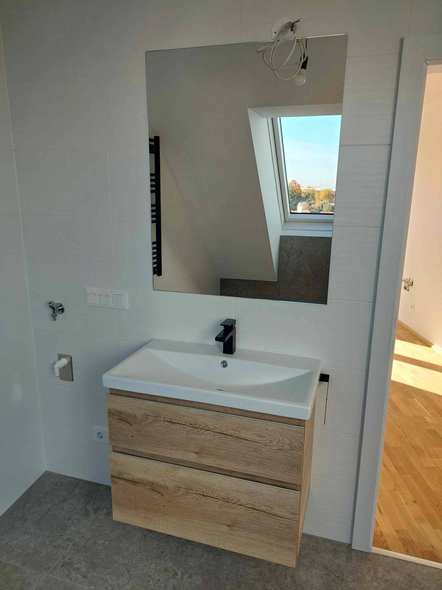 Modernes Badezimmer mit Holzwaschtisch, großem Spiegel und Fenster, das natürliches Licht hereinlässt.
