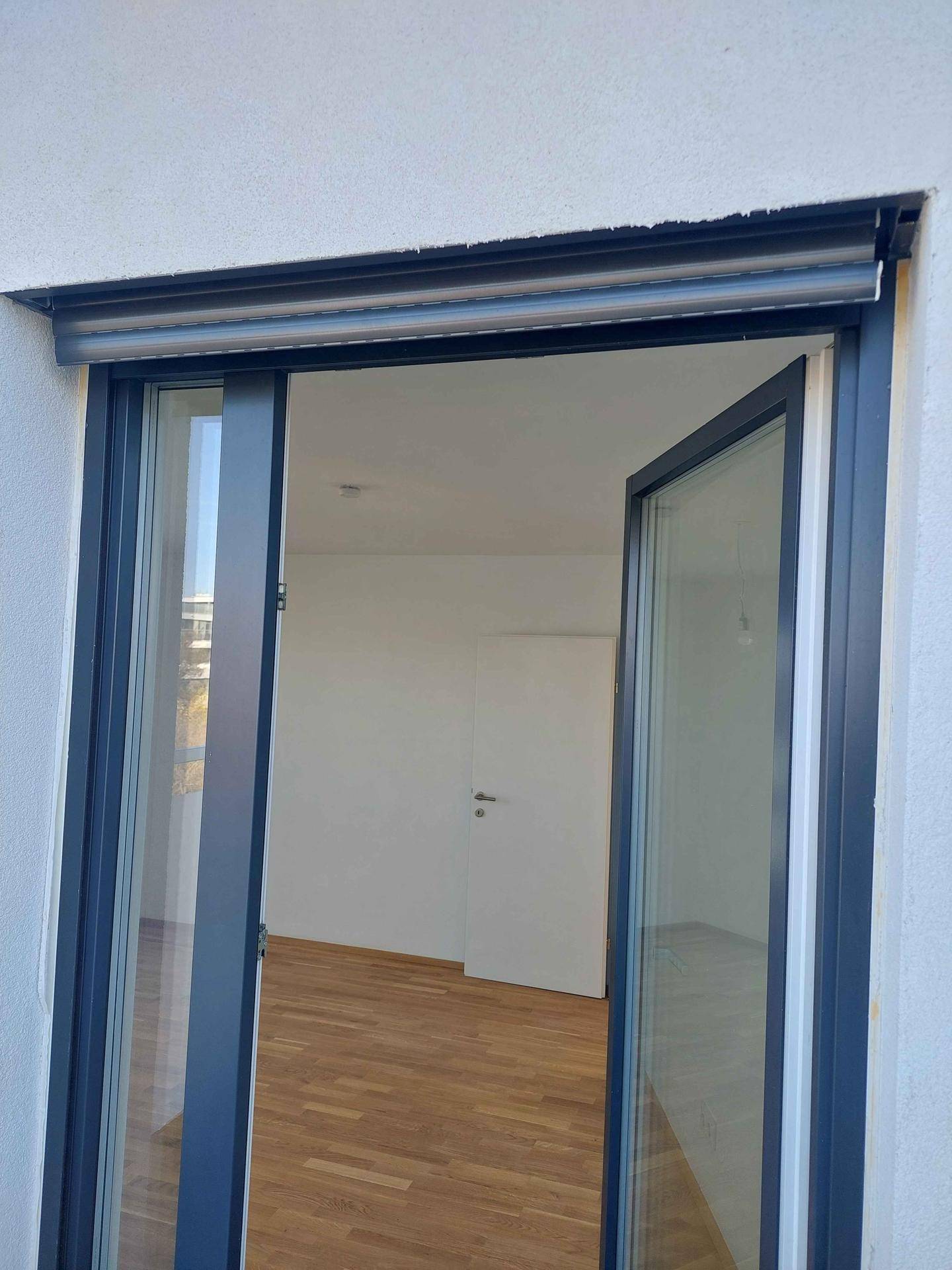 Detailansicht eines Fensters mit Rollladen, das den Blick in einen hellen Innenraum freigibt.