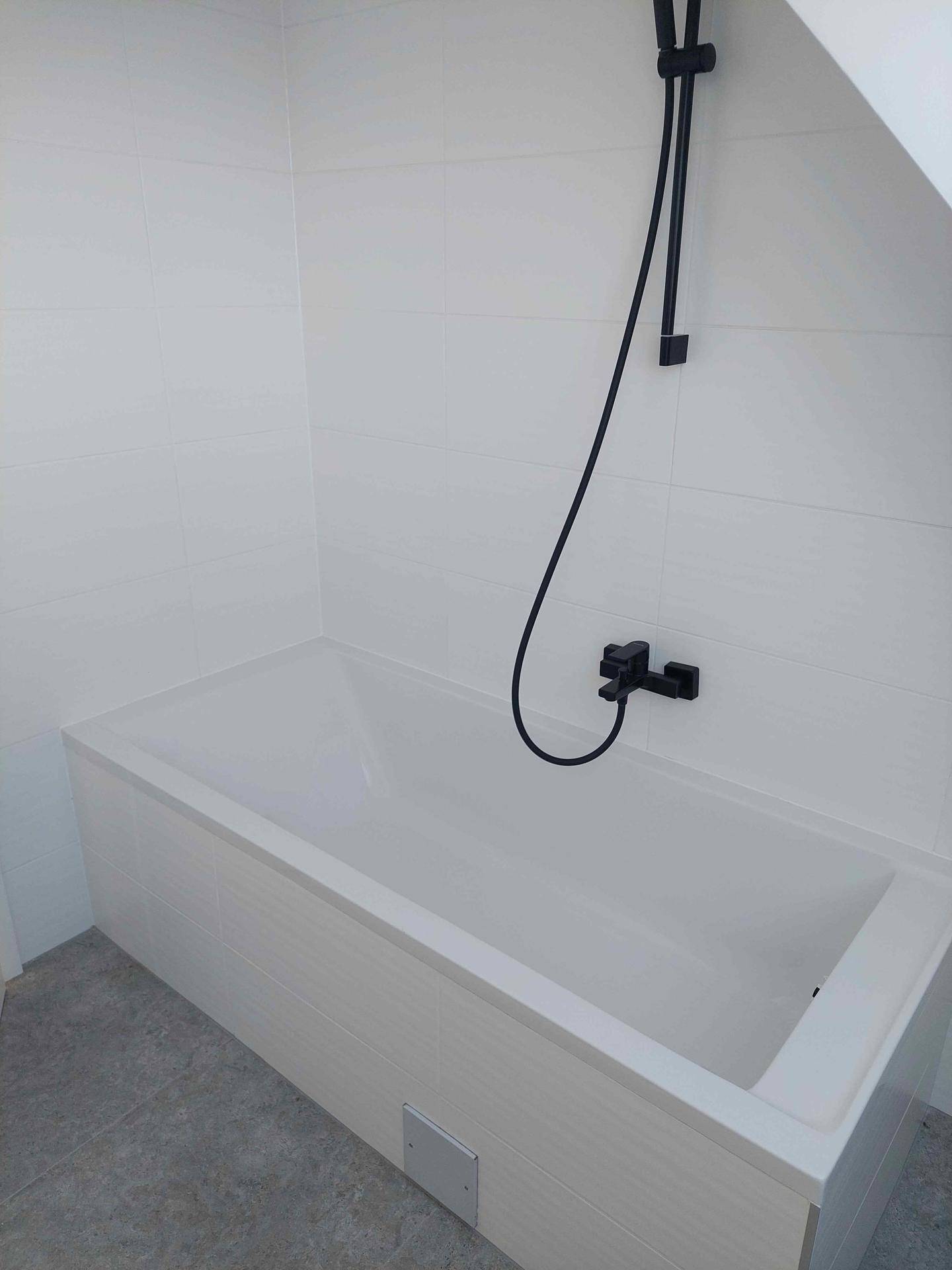 Modernes Badezimmer mit weißer Badewanne, schwarzen Armaturen und eleganten Wandfliesen unter Dachschräge.