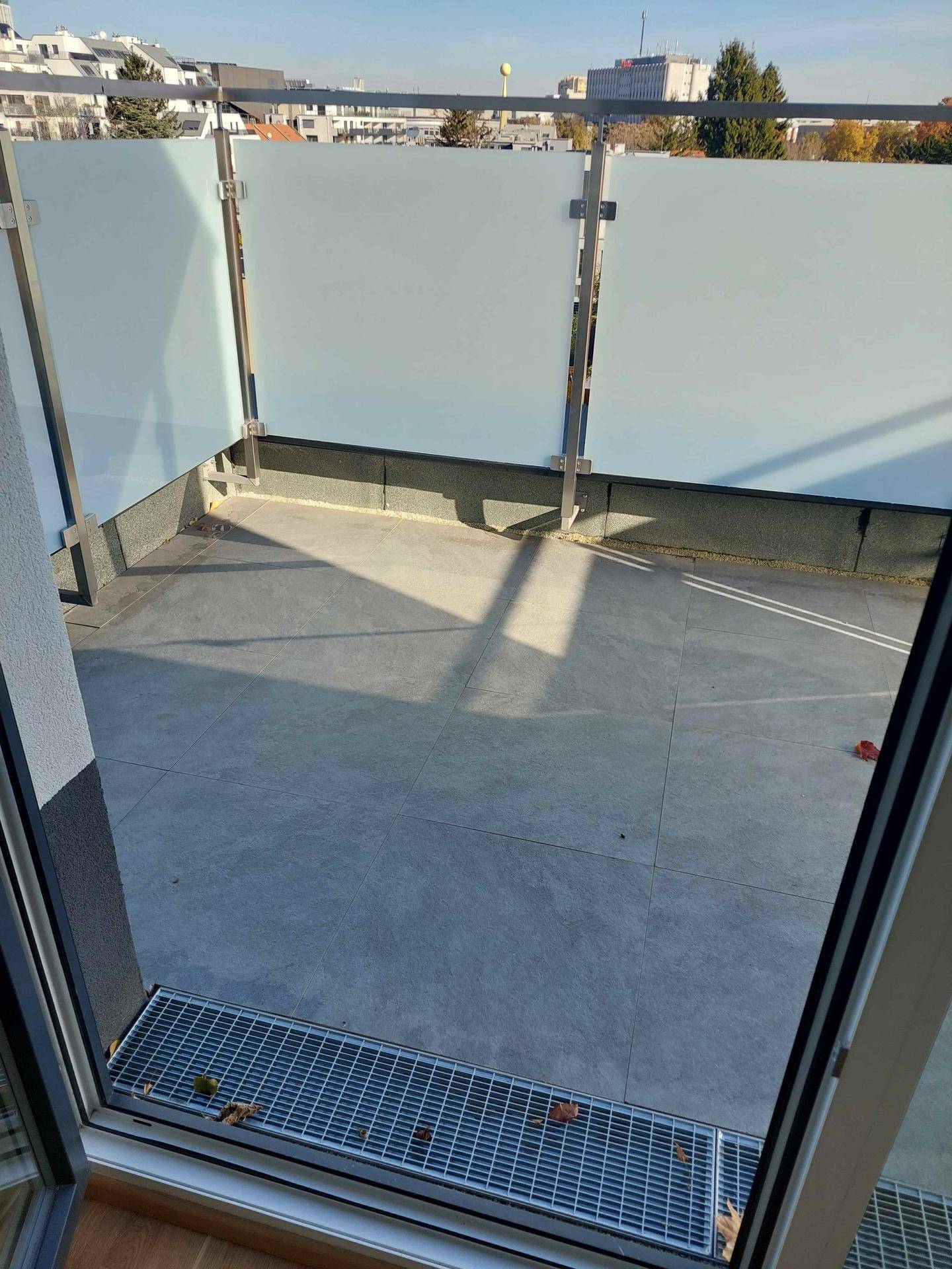 Geräumige Terrasse mit modernen Fliesen und Milchglasgeländer, ideal für entspannte Stunden im Freien.