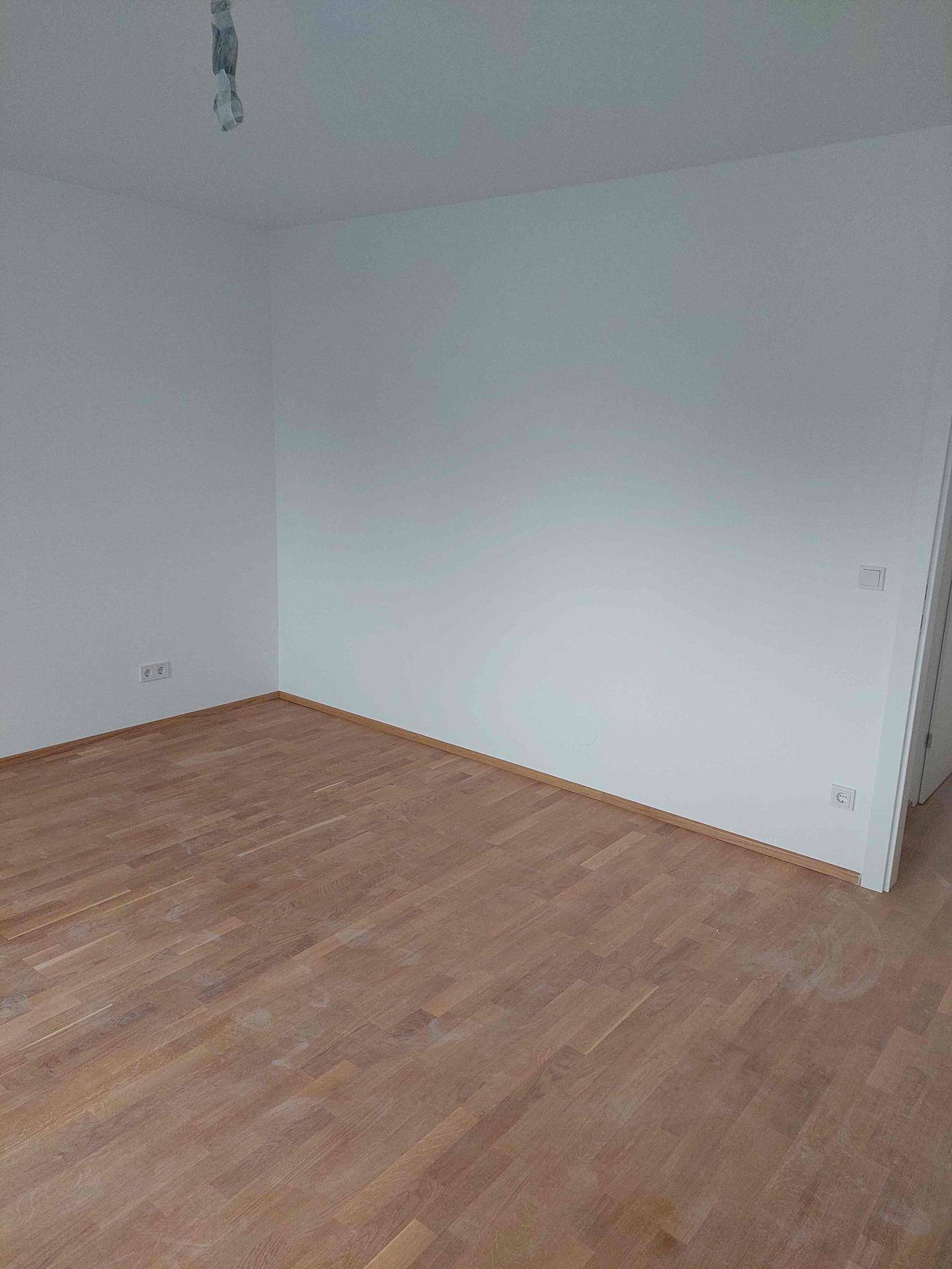 Sauberer, leerer Raum mit hellem Holzplankenboden und weißen Wänden, bereit zur individuellen Gestaltung.